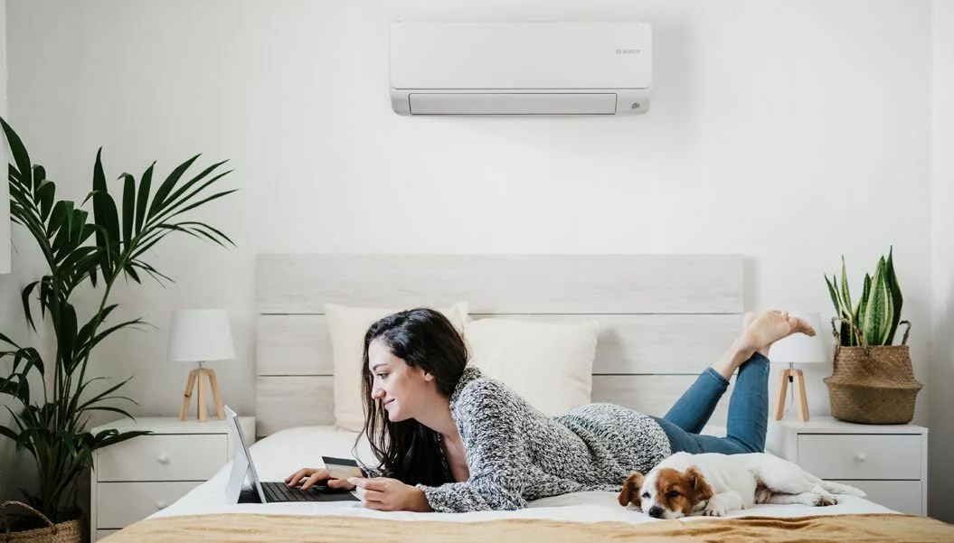 a woman lying on a bed with a dog and a laptop and airco